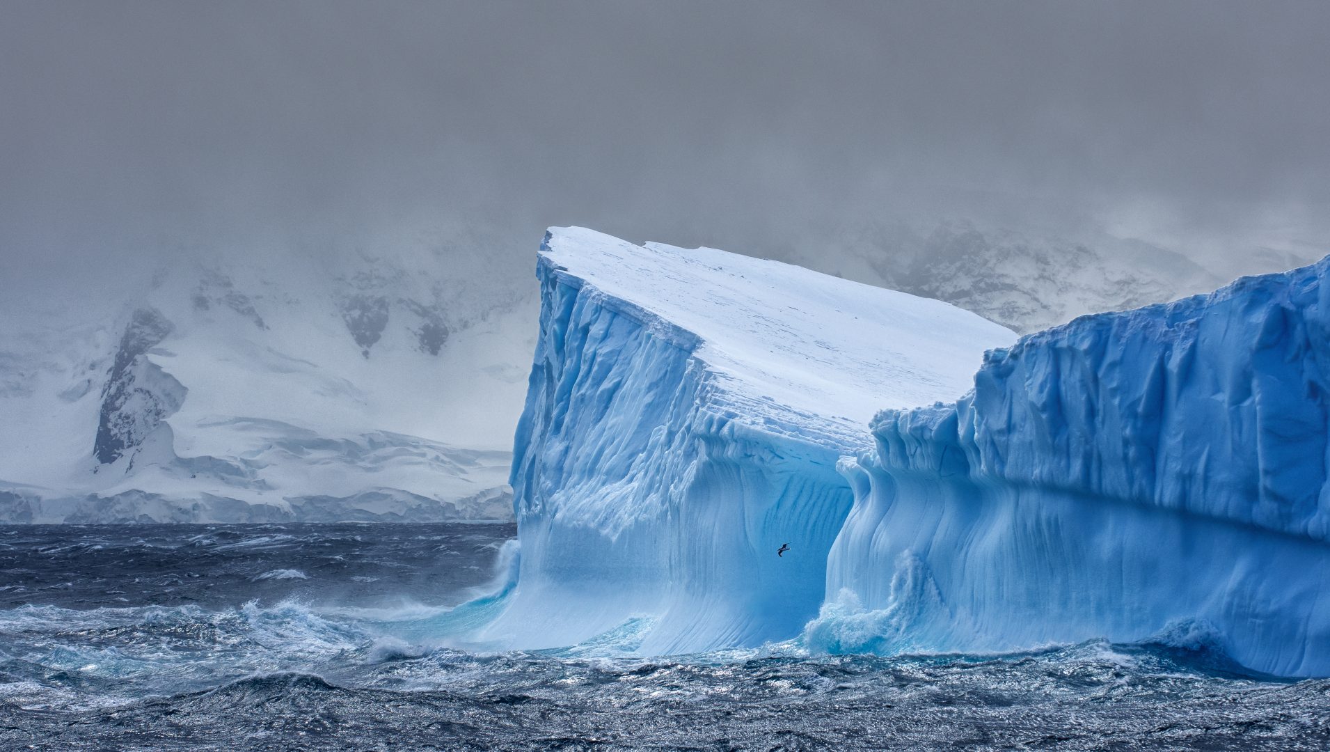Antarctica-Iceberg-with-land-behind-dramatic