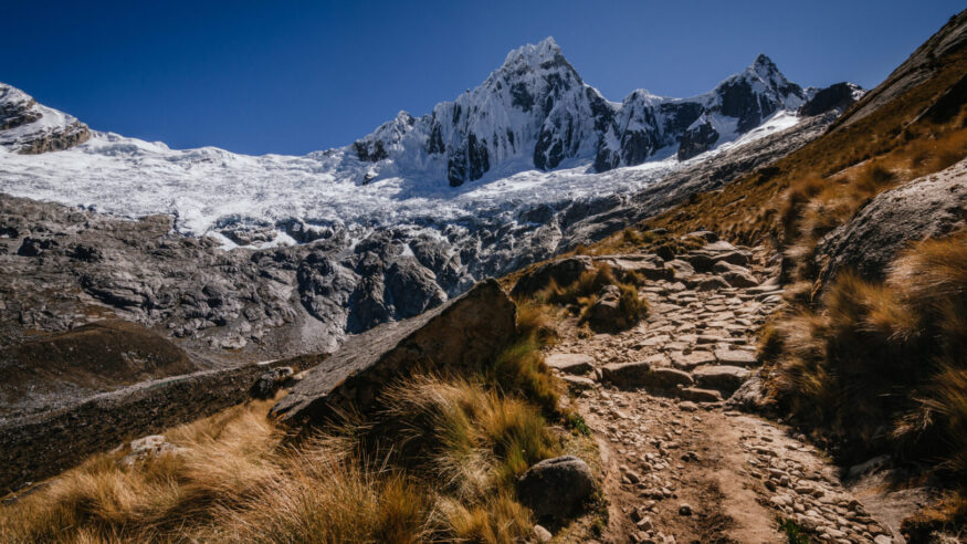 High snowy mountain of Taulliraju and path surrounded by grass in the foreground, in the quebrada santa cruz in peru