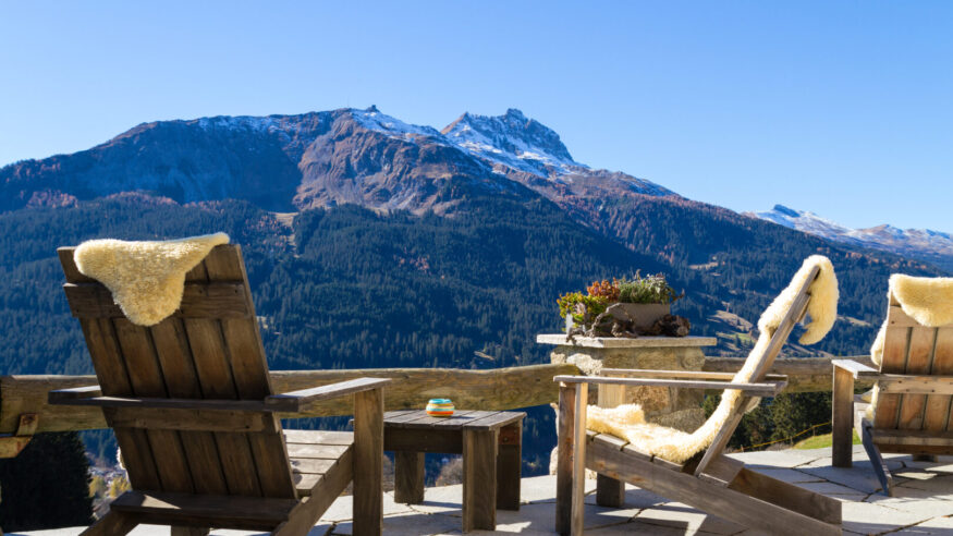 Wooden easy chairs at a mountain lodge terrace with panoramic view of beautiful alpine landscape in autumn at the Klosters - Davos region, Switzerland.